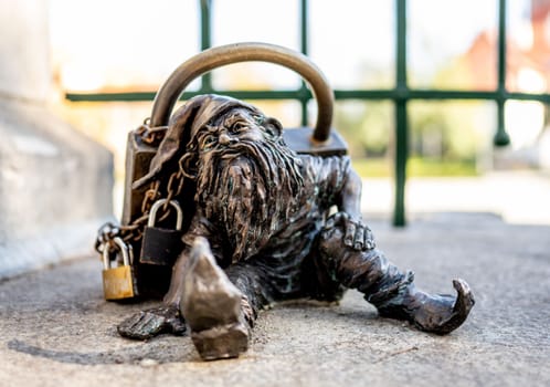 Dwarf with a padlock near bridge. Small bronze figures of gnomes on the streets of Wroclaw. Europe