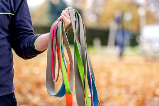 Strong man guy holding set of colorful elastic rubber bands at the stadium outdoors. Athlete male person during workout with additional sport equipmant