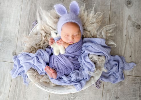 Newborn baby boy sleeping with kitty toy and smiling. Little infant child swaddled in fabric napping