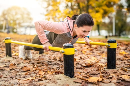 Fitness girl doing push ups outdoots in autumn time. Young woman exercising in park