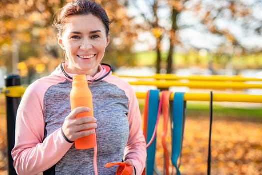 Fitness girl with bottle with water after exercising in autumn park outdoors. Young woman and hydration sport portrait at fall season