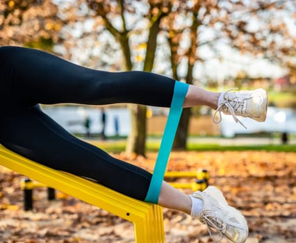 Girl making legs ezxercises with elastic rubber band at autumn time outdoors. Young woman during legs training workout