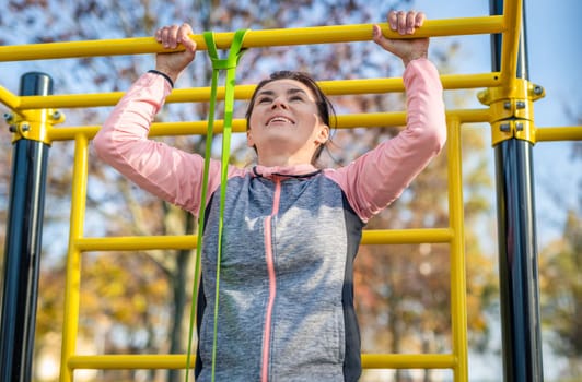 Fitness girl doing pull ups outdoots in autumn time. Young woman exercising in park for strong arms