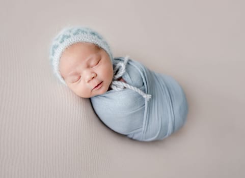 Newborn baby boy sleeping swaddled in fabric studio portrait. Infant child kid napping