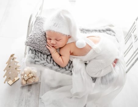 Newborn baby boy wearing knitted pants and hat sleeping on tiny bed studio portrait. Infant child kid napping on his tummy