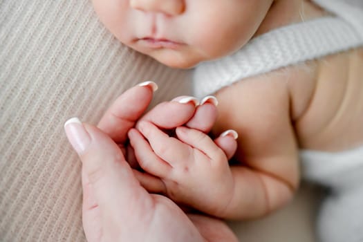 Mother hand holding tiny fingers of newborn baby boy, closeup. Infant child kid sleeping with parent mom care