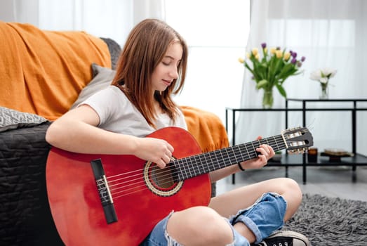 Girl teenager practicing guitar playing at home sitting on floor. Pretty guitarist with musician instrument