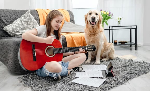 Girl teenager practicing guitar playing with golden retriever dog at home sitting on floor. Pretty guitarist with musician instrument and purebred pet doggy looking at camera