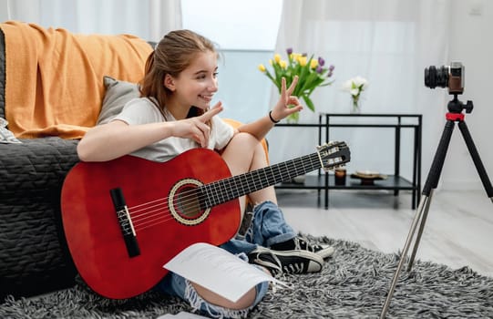 Girl teenager with guitar recording streaning online lesson with camera for blog followers in social media. Young musician guitarist filming vlog at home