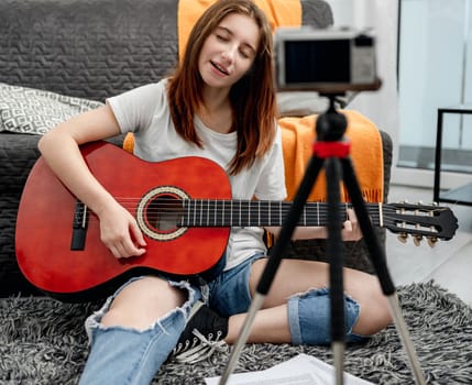 Girl teenager with guitar recording streaning online lesson with camera for blog followers in social media. Young musician guitarist filming vlog with tutorial