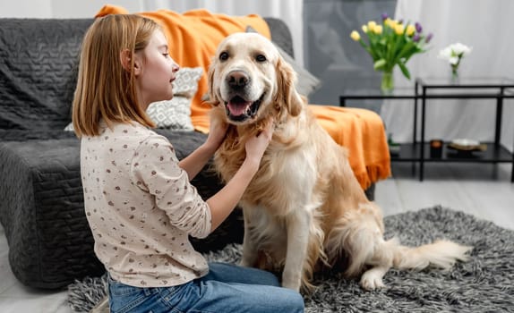 Preteen girl child petting golden retriever dog sitting on floor at home. Cute kid with purebred pet doggy labrador indoors