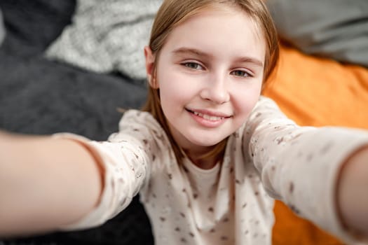 Preteen girl child portrait during making selfie at home with smartphone. Cute female kid posing and smiling for social media