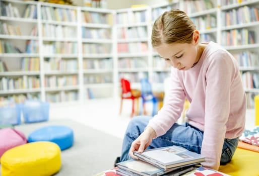 Pretty girl child reading book in library. Cute female preteen kid studying literature and making research for school in biblioteque