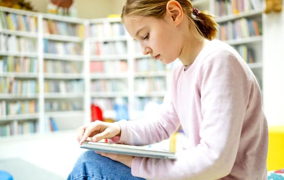 Pretty girl child reading book in library. Cute female preteen kid studying literature in biblioteque