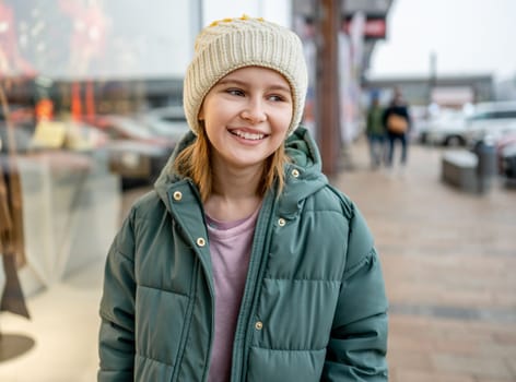 Preteen girl smiling at street portrait in city with blurred background. Cute female child kid wearing hat outdoors at autumn time