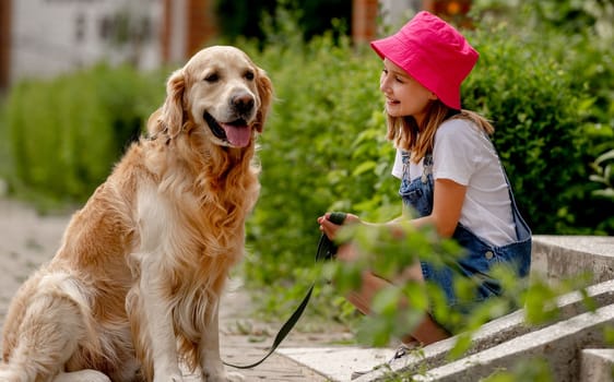Preteen girl wearing hat with golden retriever dog sitting outdoors in summertime. Pretty kid petting fluffy doggy pet in city