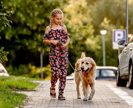 Preteen girl wearing jeans dressdoors in summertime. Pretty kid petting fluffy doggy pet in city