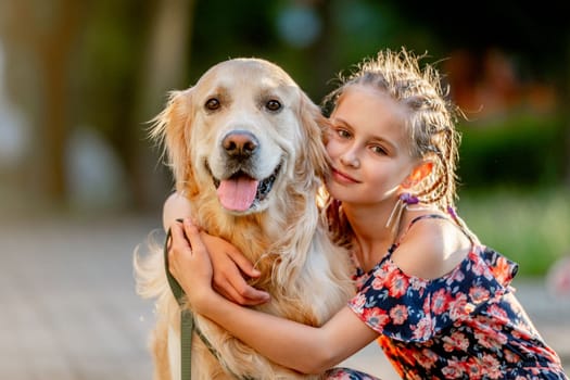 Preteen girl with golden retriever dog sitting in park in beautiful summer day. Adorable female child kid hugging purebred doggy pet outdoors portrait