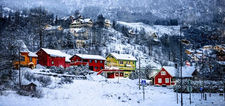 Charming village in Norway with wooden red houses surrounded with snowy mountains in winter. Scenery scandinavian landscape in Europe