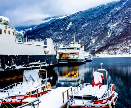 Cruise boat and traditional wooden houses in Norway surrounded with snowy mountains and cold lake in winer time. Beautiful norwegian nature, village and reflection in sea