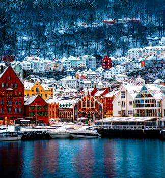 Winter Bergen city with famous Bryggen merchandise wooden houses and lights in snow season at evening. Panorama of historical harbor buildings at Christmas time