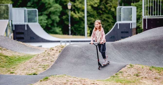 Preteen girl riding scooter in city park at spring time. Pretty child kid having fun with vehicle outdoors