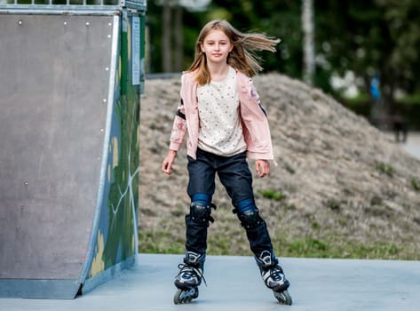 Cute girl roller skater sitting in city park on ground. Pretty female preteen kid child posing during rollerskating