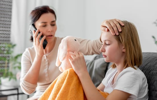 Mother with ill sick child daughter at home calling to doctor. Mom woman cares about kid with fever and virus
