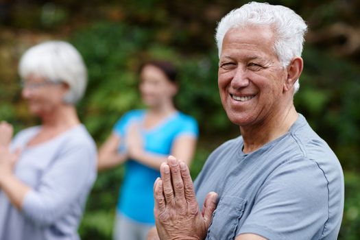 Yoga keeps me flexible even in my old age. a senior man doing yoga with other people outdoors