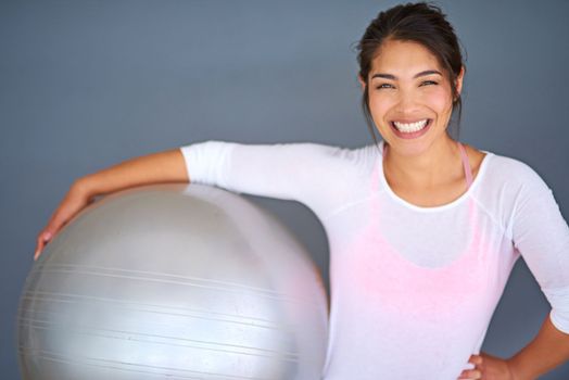 Cmon, its fun. a sporty young woman holding a pilates ball against a grey background