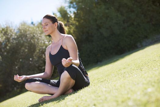 Seeking serenity. An attractive woman sitting on the grass and meditating