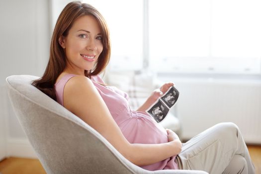 Everything is looking good. Portrait of a pretty young woman looking at her babies sonogram while sitting at home