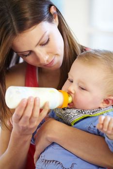 Giving him all her attention and care. Young mother bottle-feeding her baby boy