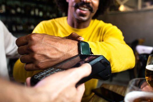 Close up of African American man paying bill with wrist watch in a restaurant. Lifestyle and technology concepts.