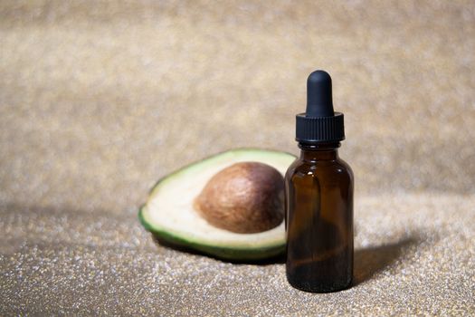 Avocado oil. Essential oil in glass bottle on shiny gold background. Avocado for healthy skin and hair. Cosmetics ingridient. Space for text.