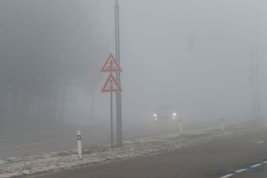 Car traveling on the foggy road with headlights or headlamps on. Low visibility - Dangerous driving of cars in winter in bad weather.