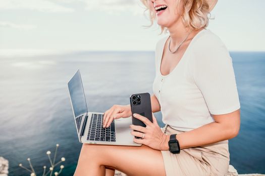 Digital nomad, Business woman working on laptop by the sea. Pretty lady typing on computer by the sea at sunset, makes a business transaction online from a distance. Freelance remote work on vacation