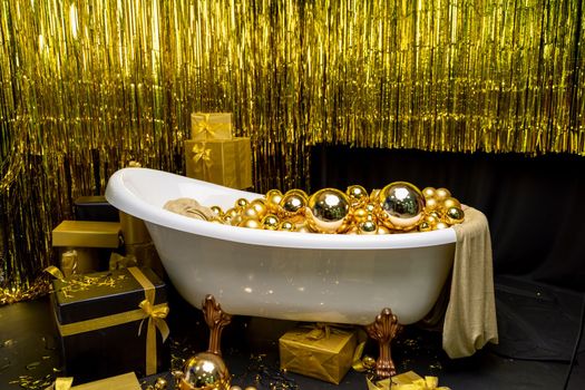 Bathtub full of golden balls. Vintage bright bathroom decorated with festive golden balls. New Year, Christmas bathroom interior