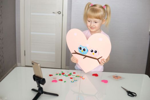 A blogger girl makes a felt craft for Valentine's Day in the shape of a heart. The concept of children's creativity and handmade