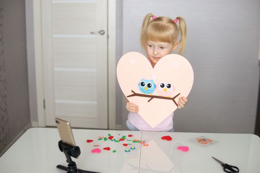 A blogger girl makes a felt craft for Valentine's Day in the shape of a heart. The concept of children's creativity and handmade