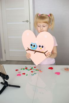 A blogger girl makes a felt craft for Valentine's Day in the shape of a heart. The concept of children's creativity and handmade