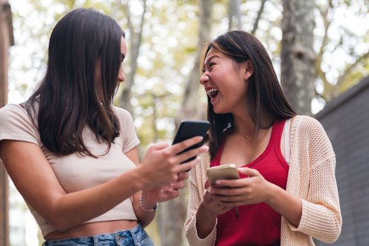 two young women laughing happy and having fun with their cell phones, concept of friendship and technology of communication