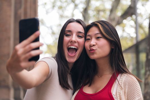 two young women smiling and having fun taking a selfie photo with a cell phone, concept of friendship and technology of communication