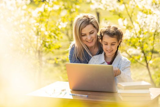 little girl with mom learning on laptop outdoor.