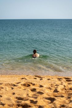 Woman sea swimsuit sand. The girl swims in the sea in a black swimsuit, the water is clean and transparent. Alone on the beach on a sunny day