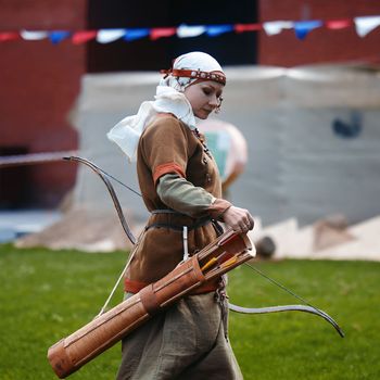 Medieval archery tournament. A woman shoots an arrow in the medieval castle yard. Woman in medieval dress with a wooden bow in her hands. historical reconstruction. 14.05,2022. Yoshkar-Ola, Russia.