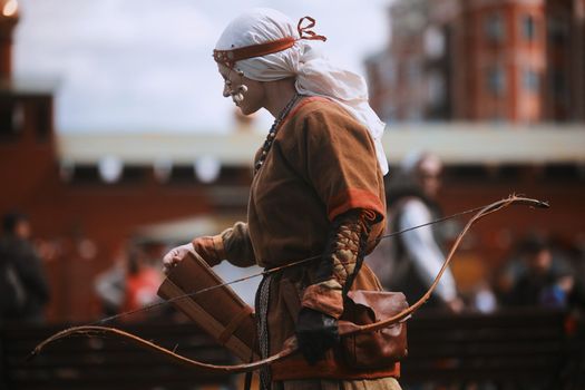 Medieval archery tournament. A woman shoots an arrow in the medieval castle yard. Woman in medieval dress with a wooden bow in her hands. historical reconstruction. 14.05,2022. Yoshkar-Ola, Russia.