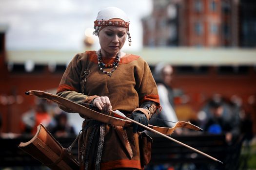 Medieval archery tournament. A woman shoots an arrow in the medieval castle yard. Woman in medieval dress with a wooden bow in her hands. historical reconstruction. 14.05,2022. Yoshkar-Ola, Russia.