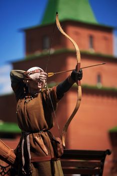 Medieval archery tournament. A woman shoots an arrow in the medieval castle yard. Woman in medieval dress with a wooden bow in her hands. historical reconstruction. 14.05,2022. Yoshkar-Ola, Russia.