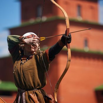Medieval archery tournament. A woman shoots an arrow in the medieval castle yard. Woman in medieval dress with a wooden bow in her hands. historical reconstruction. 14.05,2022. Yoshkar-Ola, Russia.
